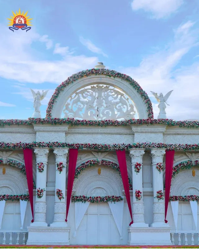 FRP floral arch with pediment, red drapes and angel statues for a marriage garden